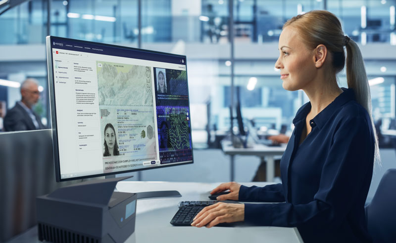 Real-time-identity-verification woman sitting at desk using a scanner to verirfy an ID document, with the document shown on screen.